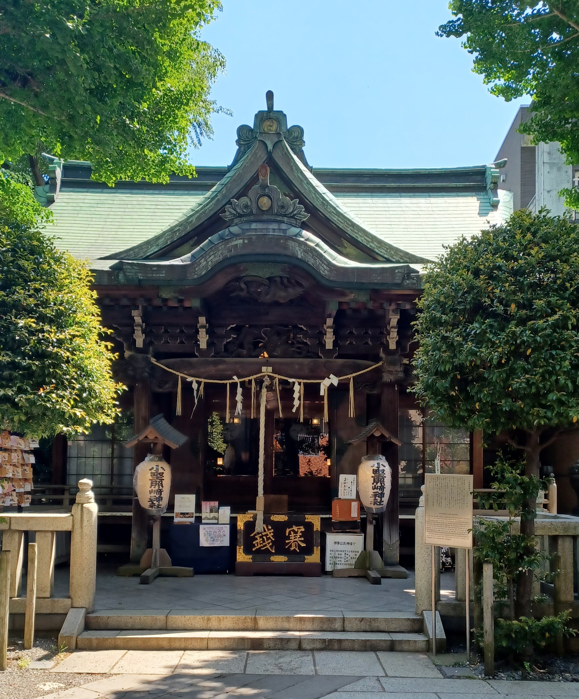 A dark brown shrine building with two beige lanterns on the left and right side with a vertical thick rope that people pull before praying.