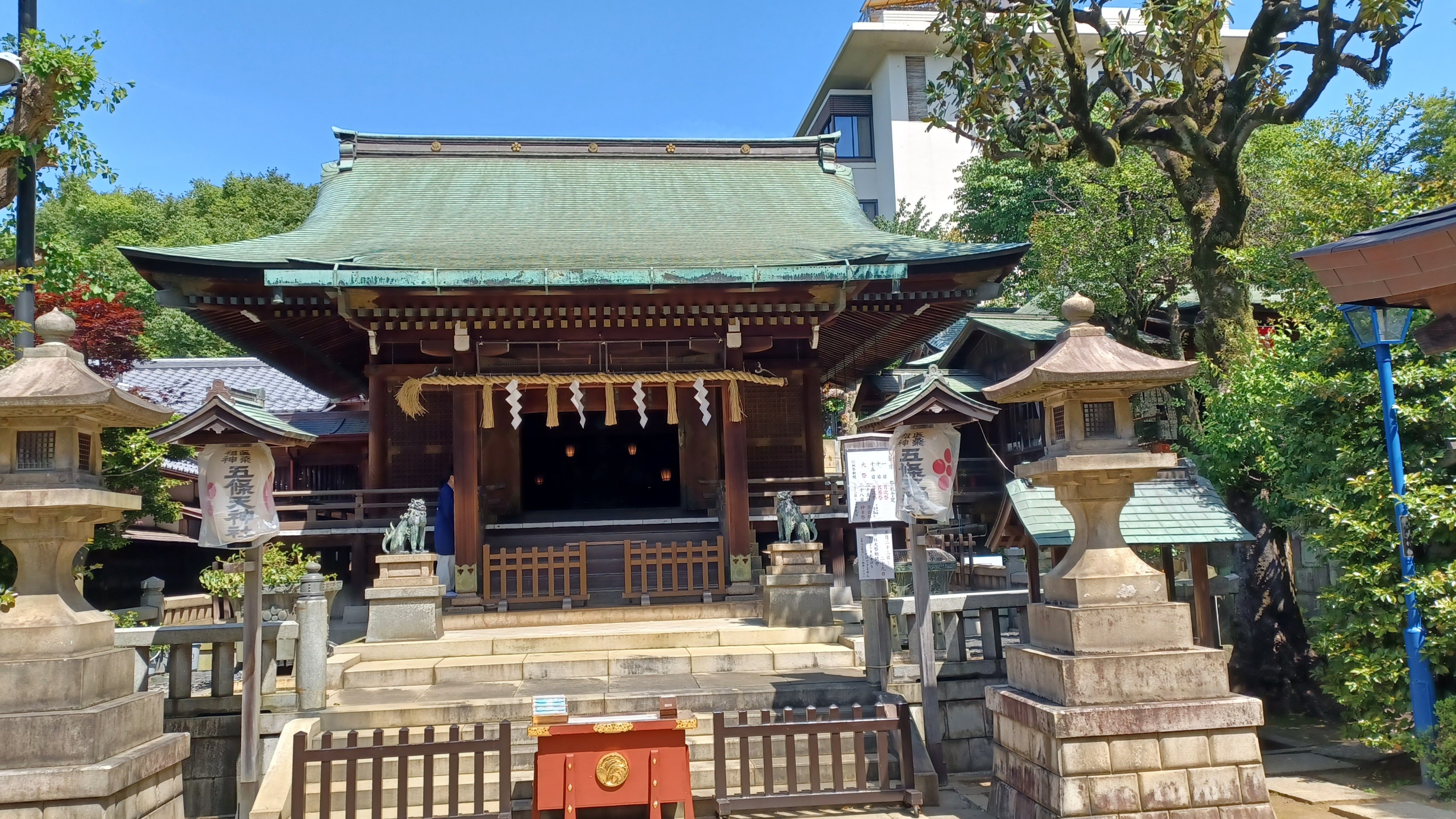 A dark brown shrine with a yellow rope above the prayer area (put up horizontally). There are stone lanterns on the left and right side in front of the building.