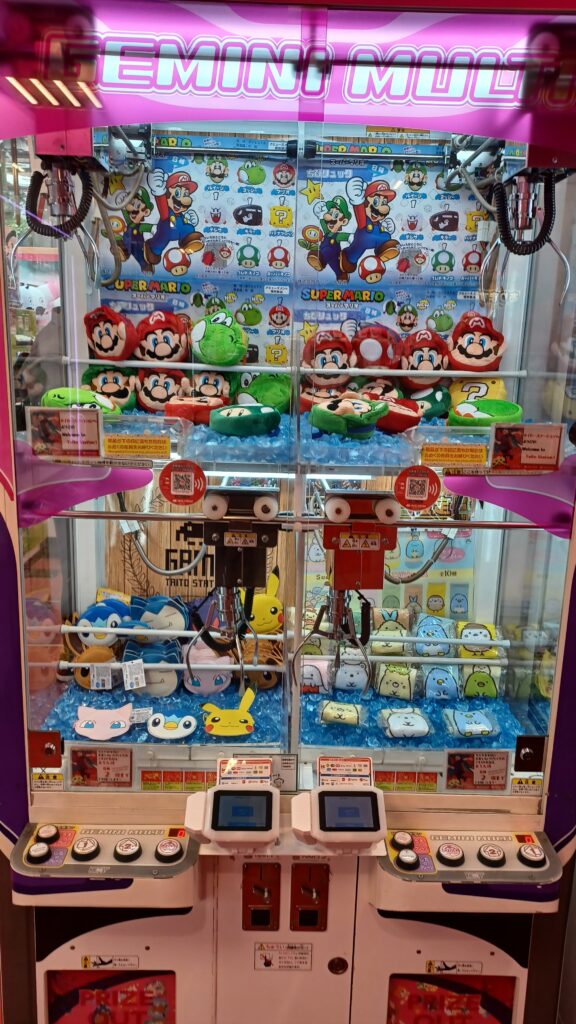 An UFO catcher machine with Mario plush characters at the top, and Pokémon plush characters at the bottom.