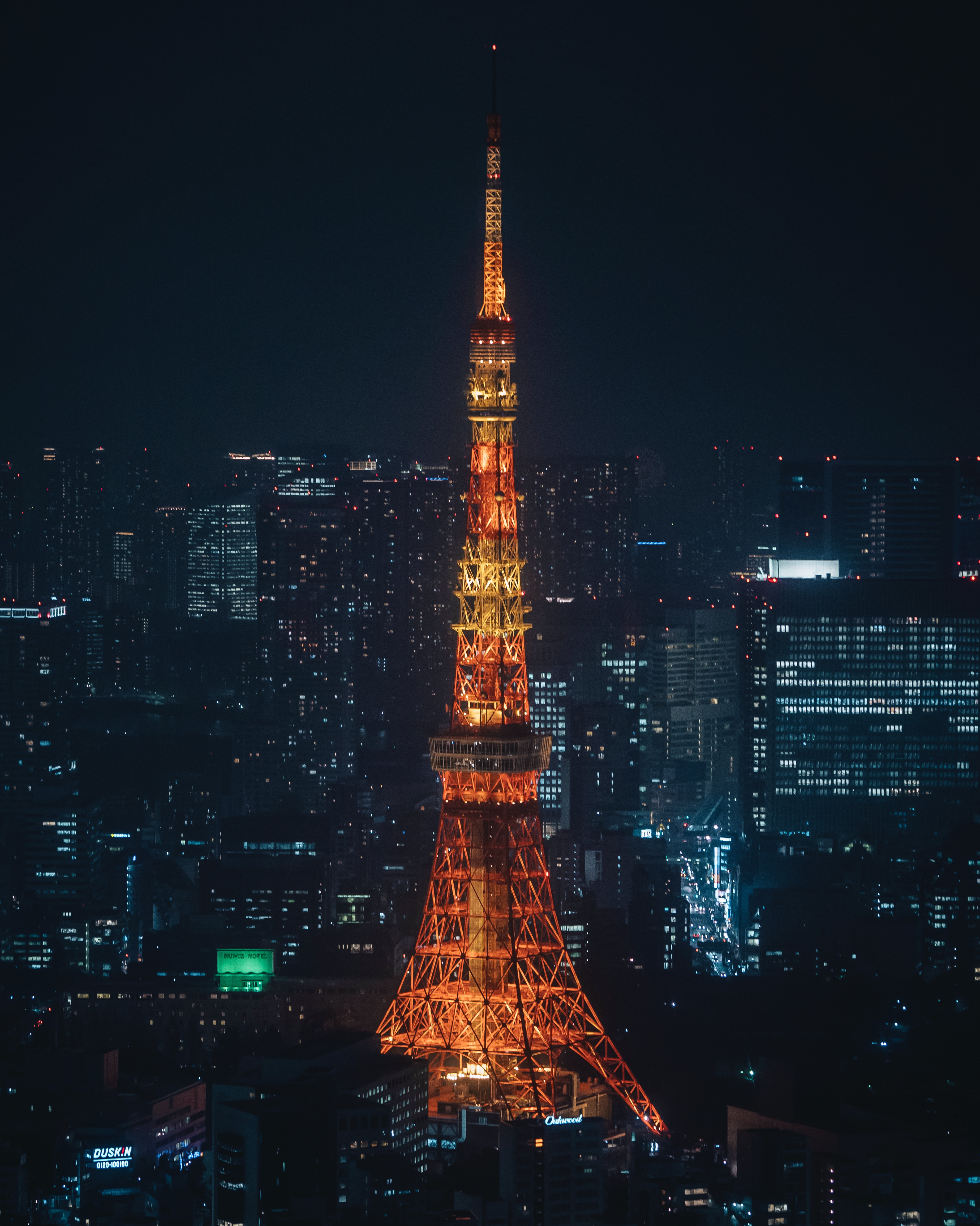 Tokyo Tower lighted in various colours at night, including yellow, orange, and red and light brown. It looks very similar to the Eiffel Tower in Paris.