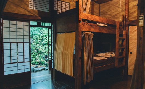 A dorm bedroom with a dark brown wooden bunk bed, wooden floor, and a Japanese-style sliding door that leads to the Zen garden.