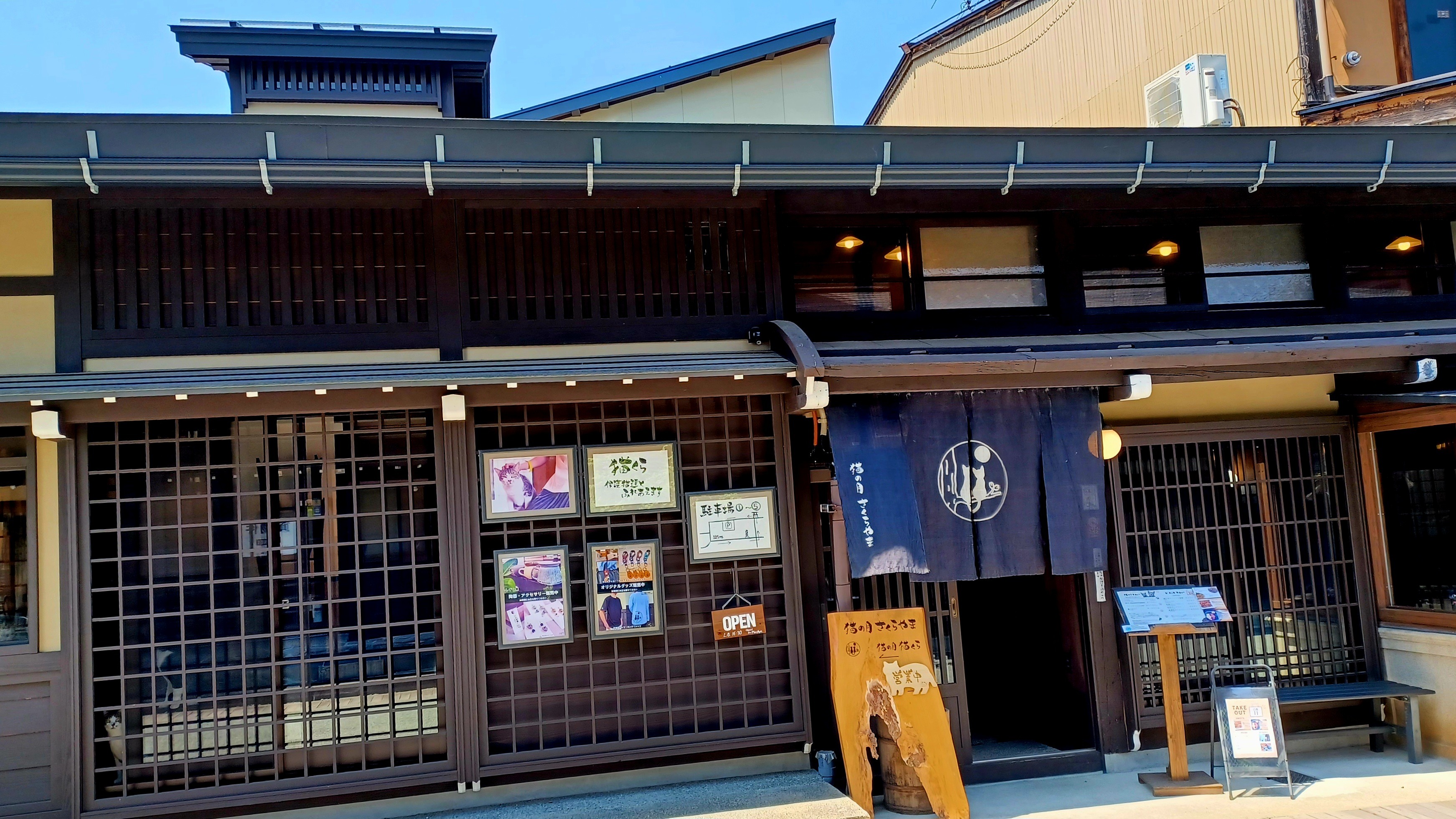 A dark brown wooden traditional Japanese house with some posters on the sliding door, and a black entrance flag where you enter the cat cafe.