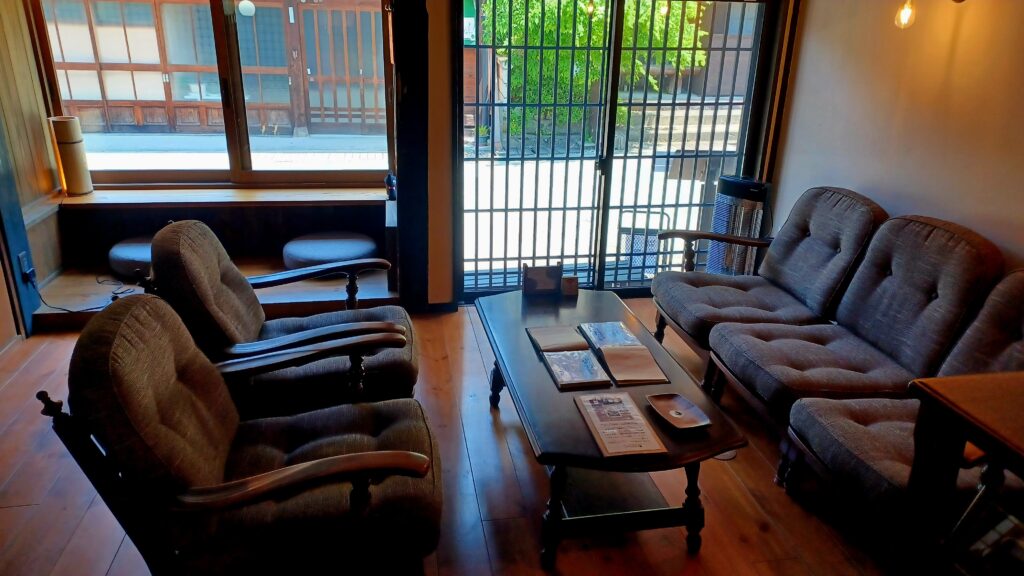 A cozy sitting area with 5 brown/grey armchairs and a dark brown coffee table in the middle. There are some books and a menu on the table. The sitting area is right next to the see-through sliding door, so you can look outside.