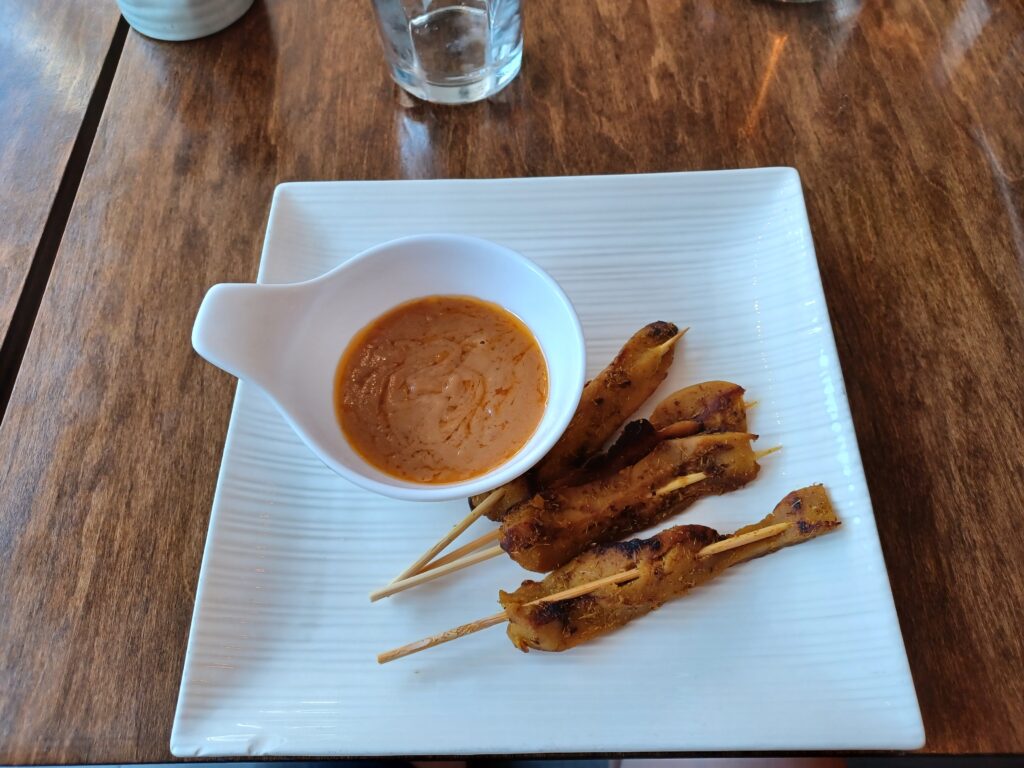 Four soy chicken skewers with an orange Thai peanut sauce on the side.