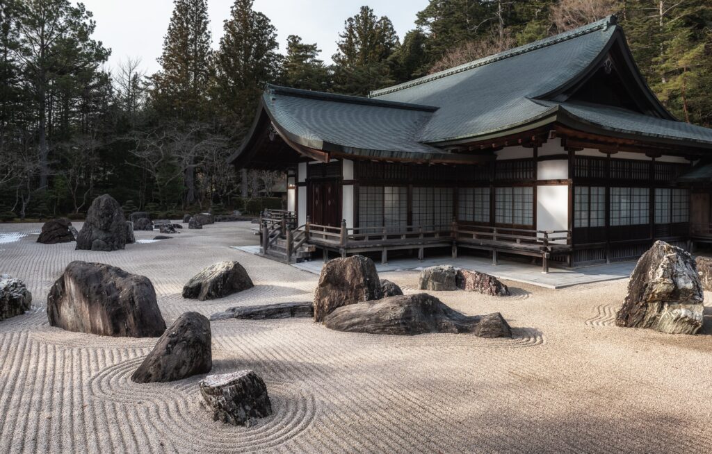 A garden of large rocks in front of a dark brown and white temple building. 