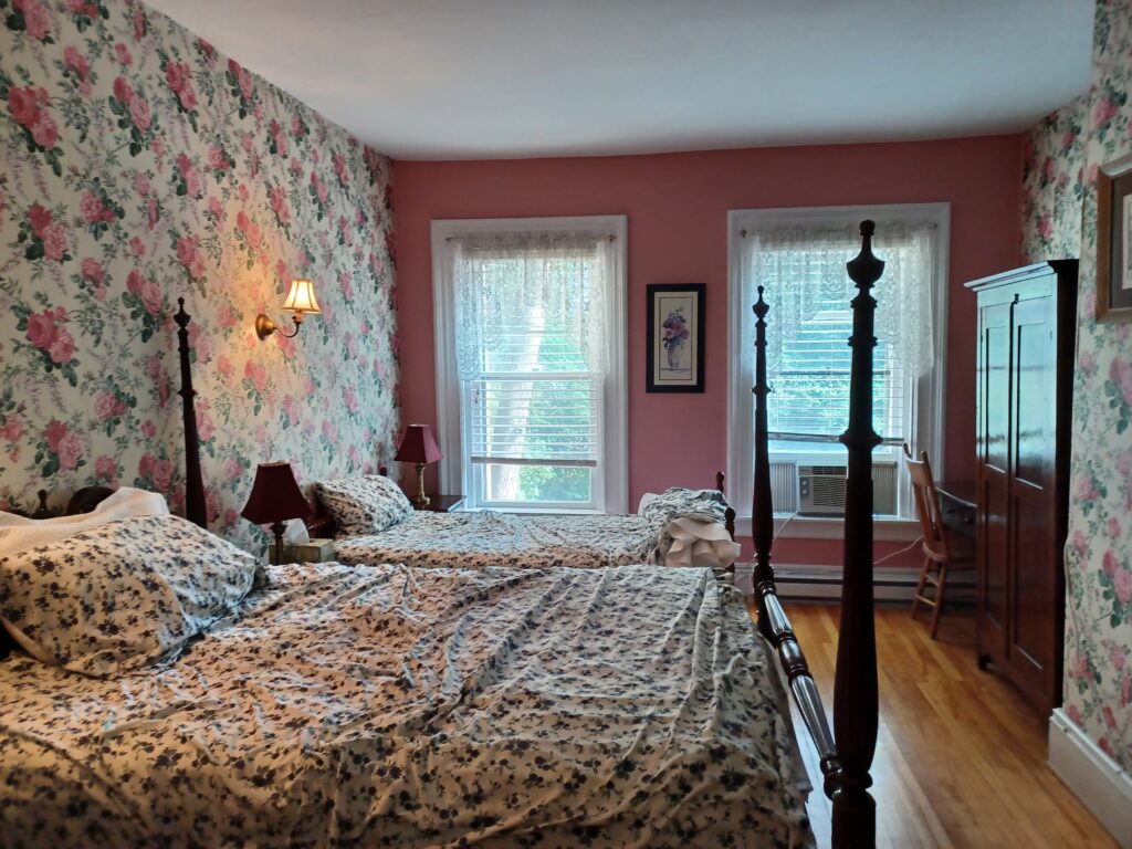 A pretty bed room with pink /flower covered walls and two beds with high corners on the left. On the right, there's a high dark brown closet.