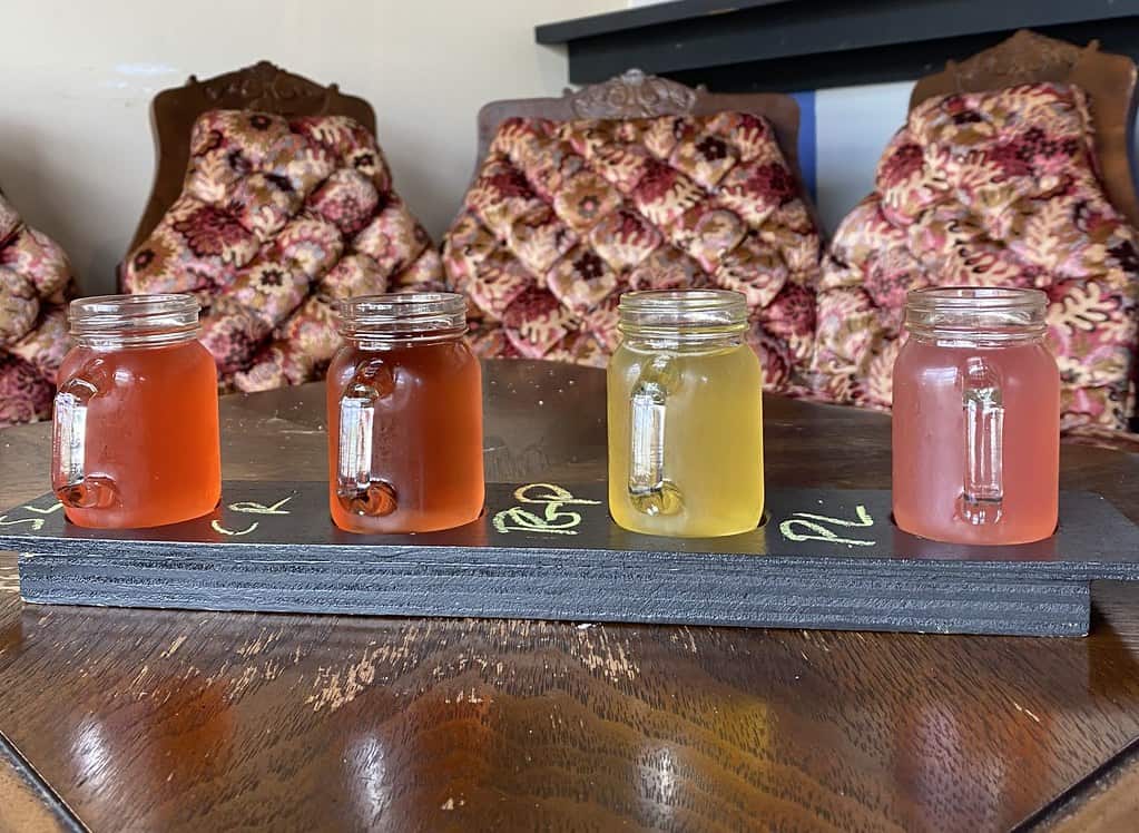 A selection of four cider drinks with different colours (light red, dark red, yellow, and pink) standing next to each other on a table.