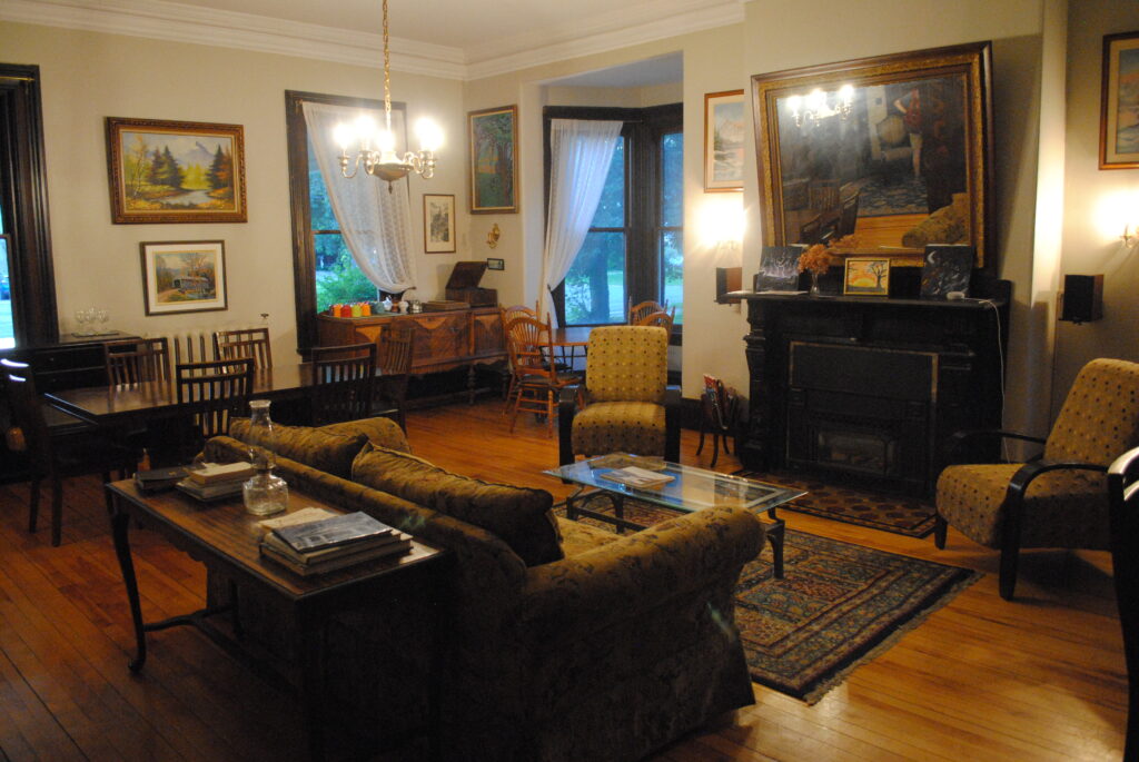 An elegant dining room with a couch, chairs, armchair, paintings on the wall, small coffee table, and a rug, and a wood stove.