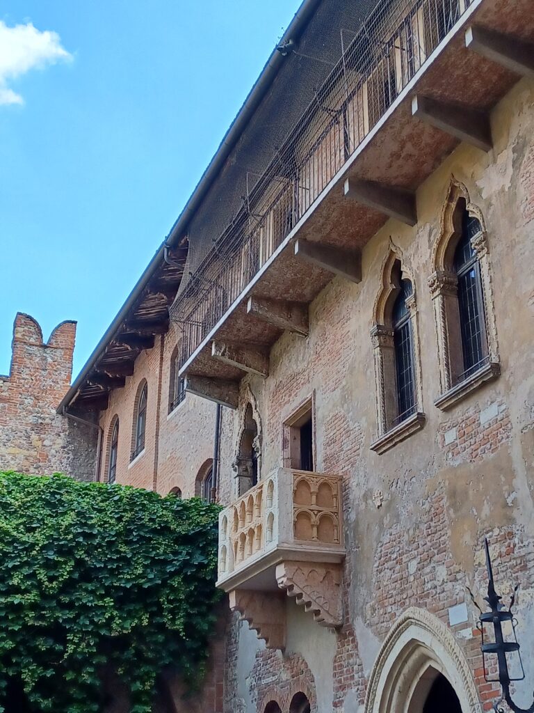 A beautiful beige stone balcony of a brick house next to a green tree. There are two triangular shaped rocks on both sides of the balcony to support it. 