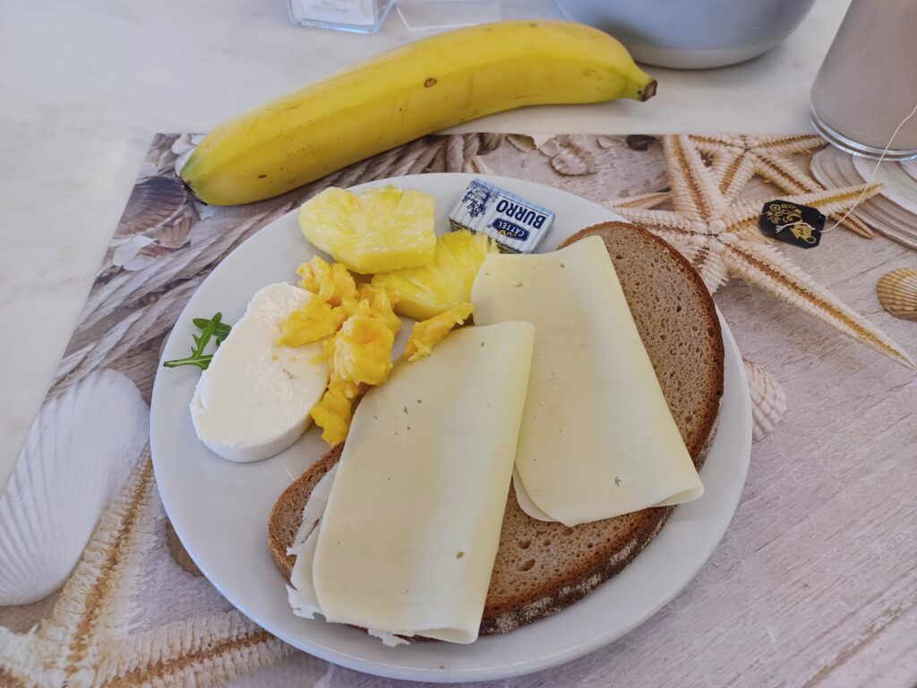 A plate of breakfast food: cheese on bread, pineapple, scrambled eggs, mozzarella cheese, and a banana.