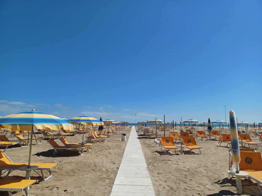 A white sandy beach with yellow/blue sunshades and empty orange deckchairs. There's a smooth pathway in the middle for wheelchair users to get to the beach.