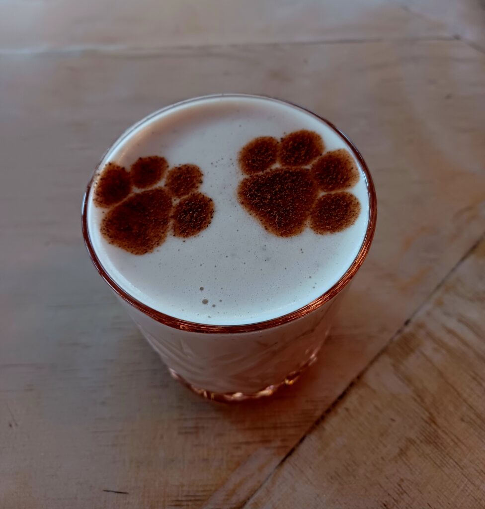 Chai tea latte in a glass with two brown paw prints on it.