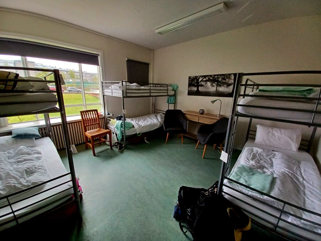 A 6-bed hostel dorm with a turquoise floor, a wooden chair and table. There's a picture on the wall as well. 