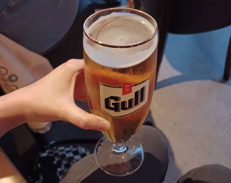 Me holding a glass of "Gull" beer. It's a light beer with a bit of foam at the top. 