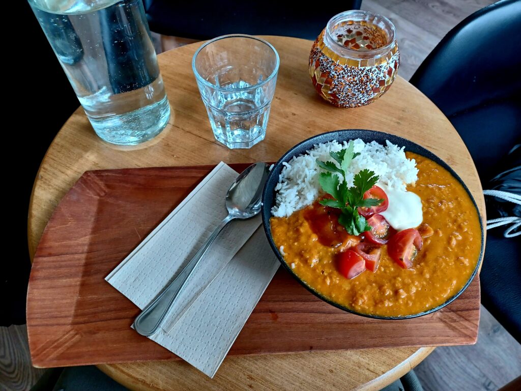 A bowl of vegan dhal, with rice, cherry tomatoes, and a tiny bit of vegan yoghurt at the top.