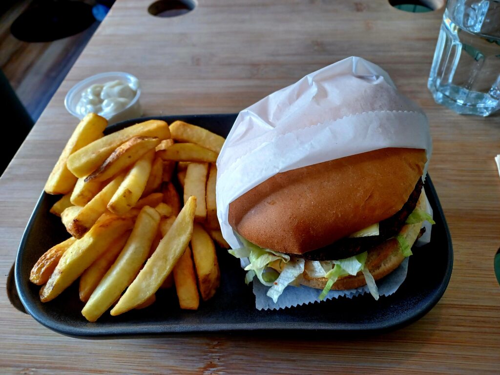 A vegetarian burger in a paper wrapping and a large portion of chips (fries) on the left side. Both are on a black tray and there's mayonnaise on the side as well. 