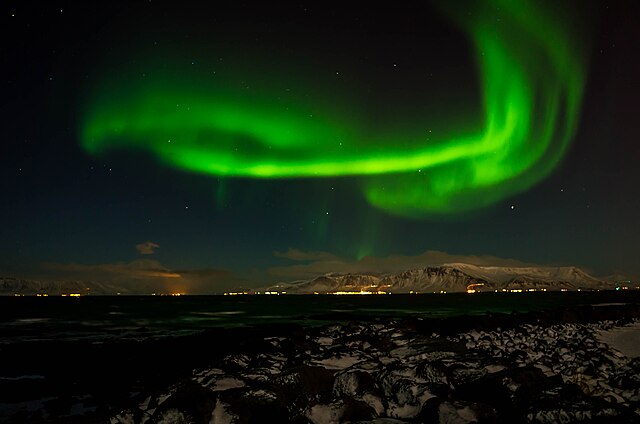 The city of Reykjavik at night with neon green Northern lights "dancing" around the dark sky.